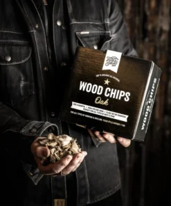 Holy Smoke Wood Chips Eiche – Räucherchips in der Hand vor dunklem Hintergrund
