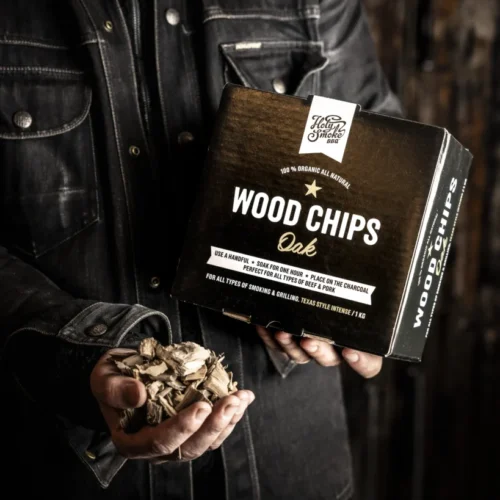 Holy Smoke Wood Chips Eiche – Räucherchips in der Hand vor dunklem Hintergrund